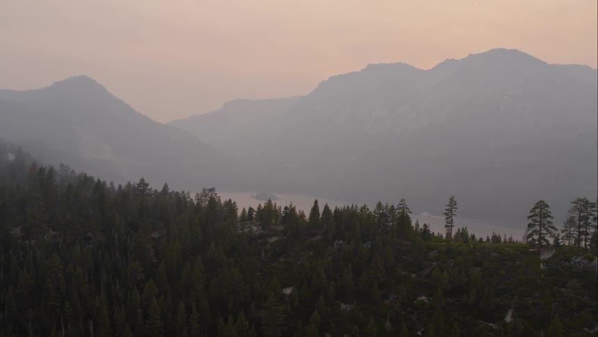 A forest and mountain range with a river running through the canyon during dawn