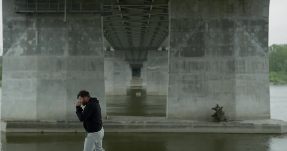 Man in black hoodie practices punching and trains alone under the bridge next to the river