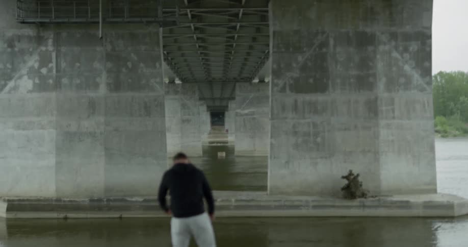 Man in black hoodie warms up next to the river under the bridge on a cloudy day