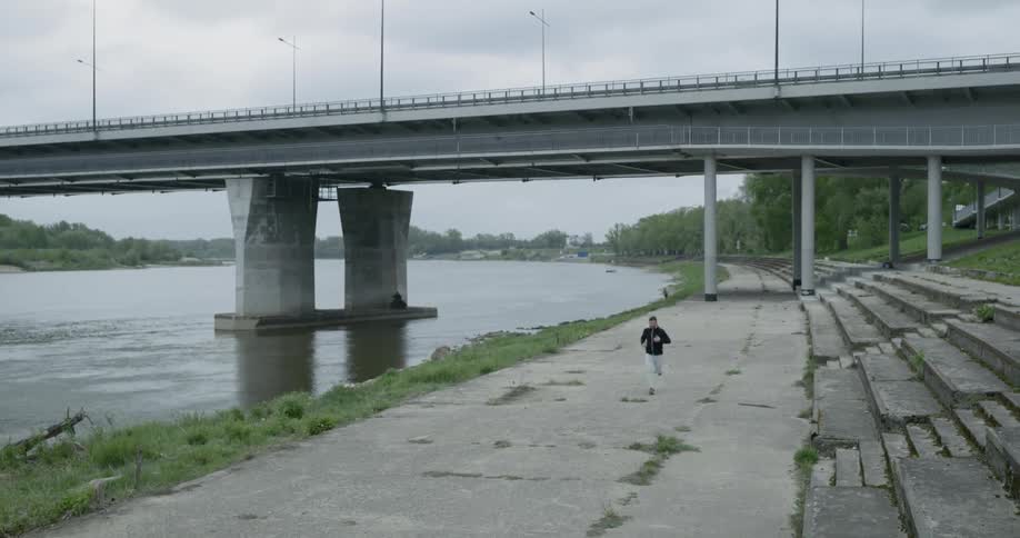 A man jogs on a pathway beside a river and a bridge
