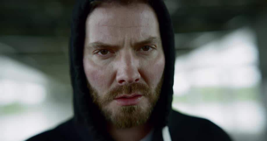 Bearded man wearing black hoodie looks at the camera angrily in the building