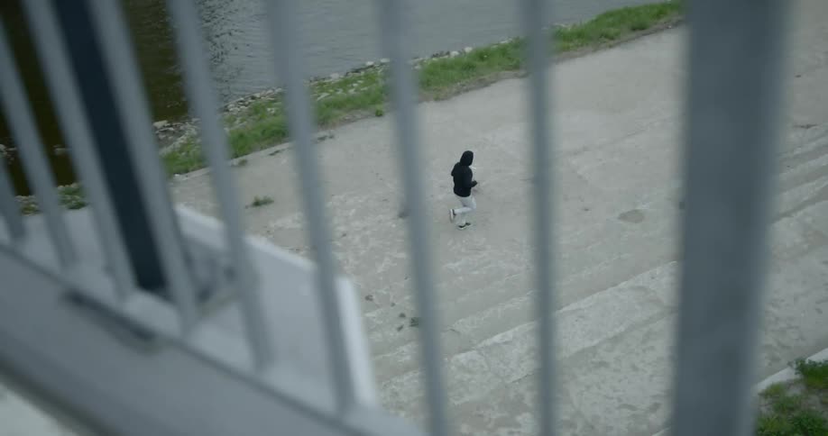 From an overpass above a person can be seen jogging on a concrete bath next to a river