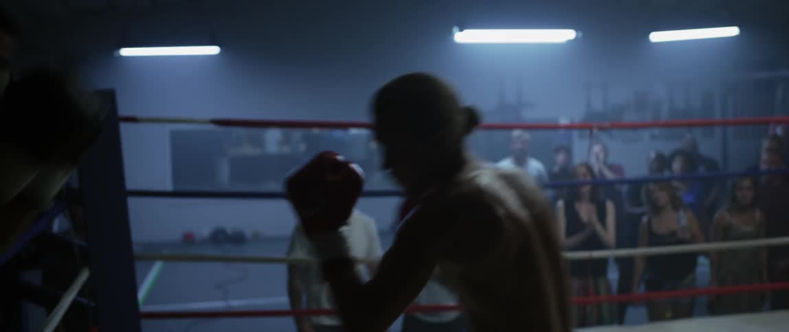 Boxers fight in a boxing ring while people watch