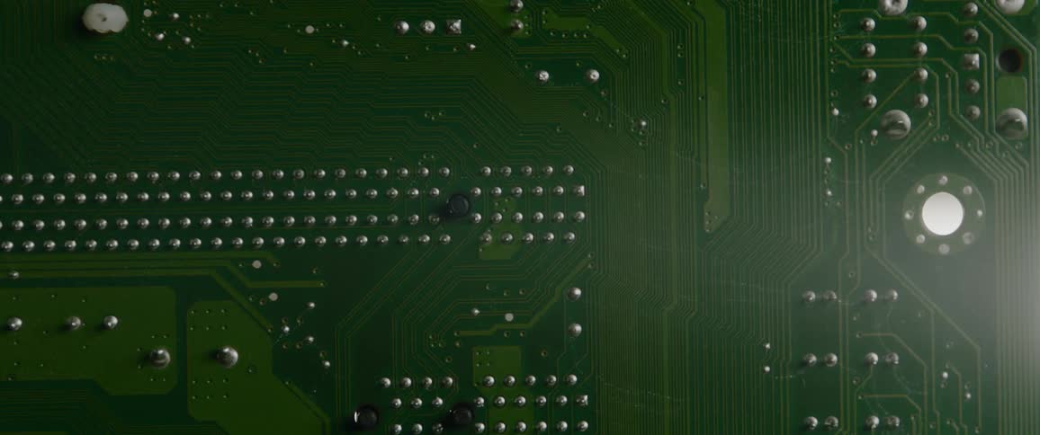 A closeup of a green printed circuit board shows numerous printed circuits and points where components are embedded