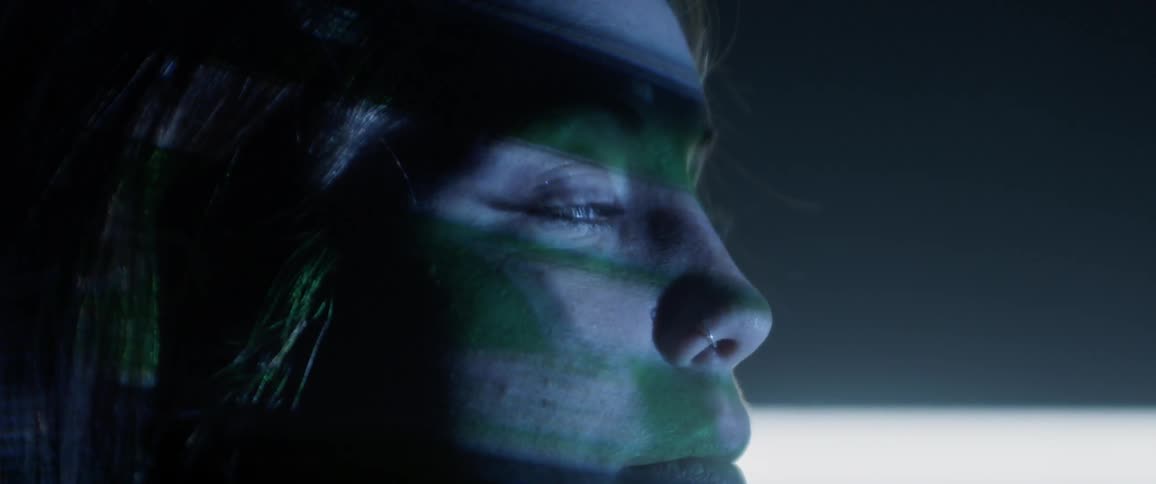 A woman standing in a dark room with images projected on her face