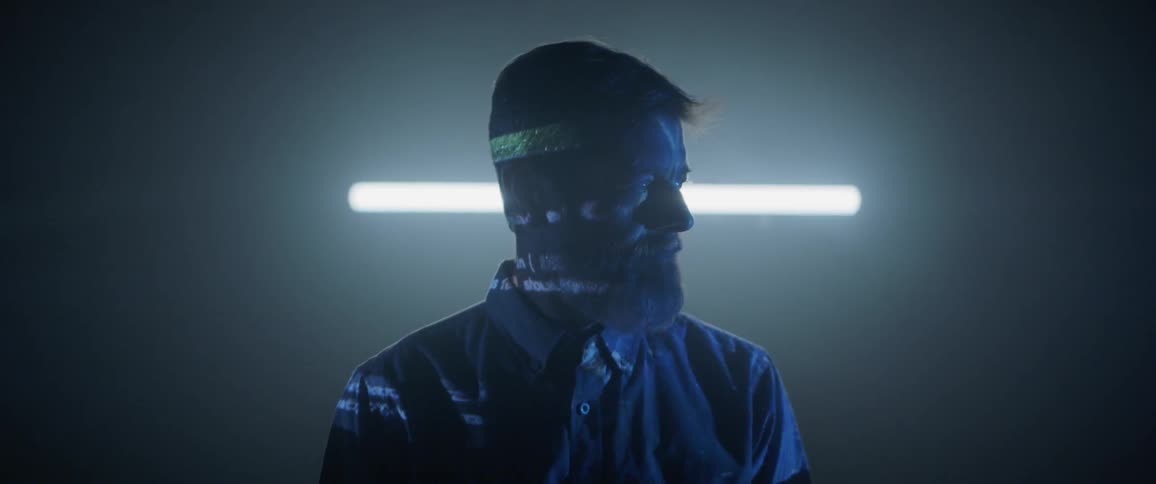 A man sits in a dark room as lights flash and reflect on him