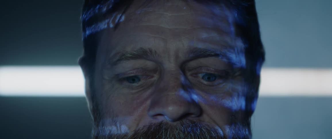 A man looks down while lights and text are projected on his face