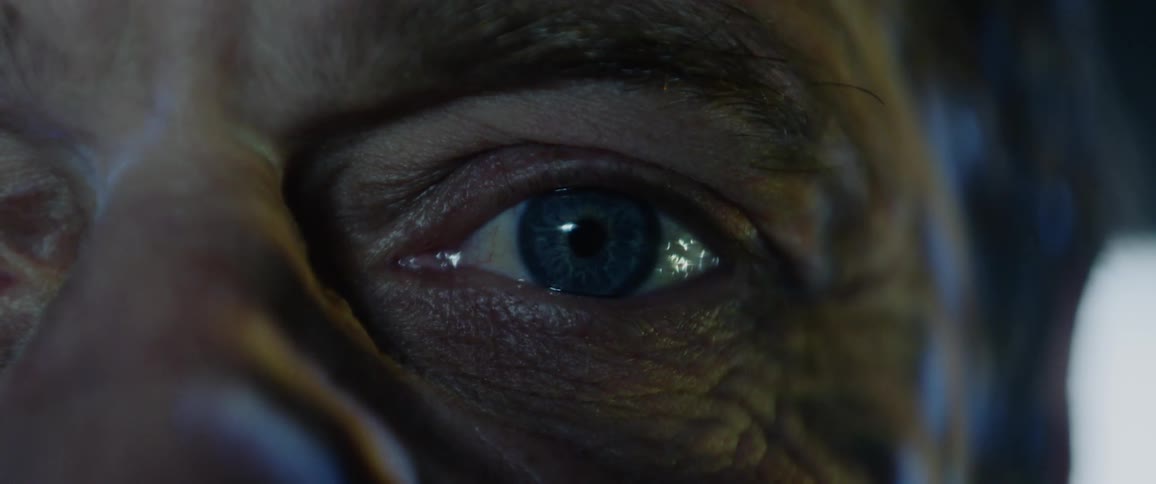 A man stares into the camera while lights are projected onto his face