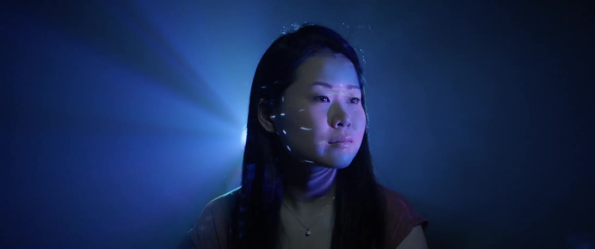 An asian girl sits and looks ahead as light flash and reflect on her