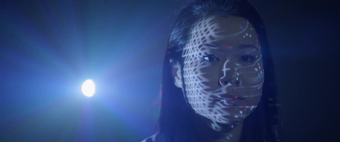 An asian woman stares ahead while bright lights flash