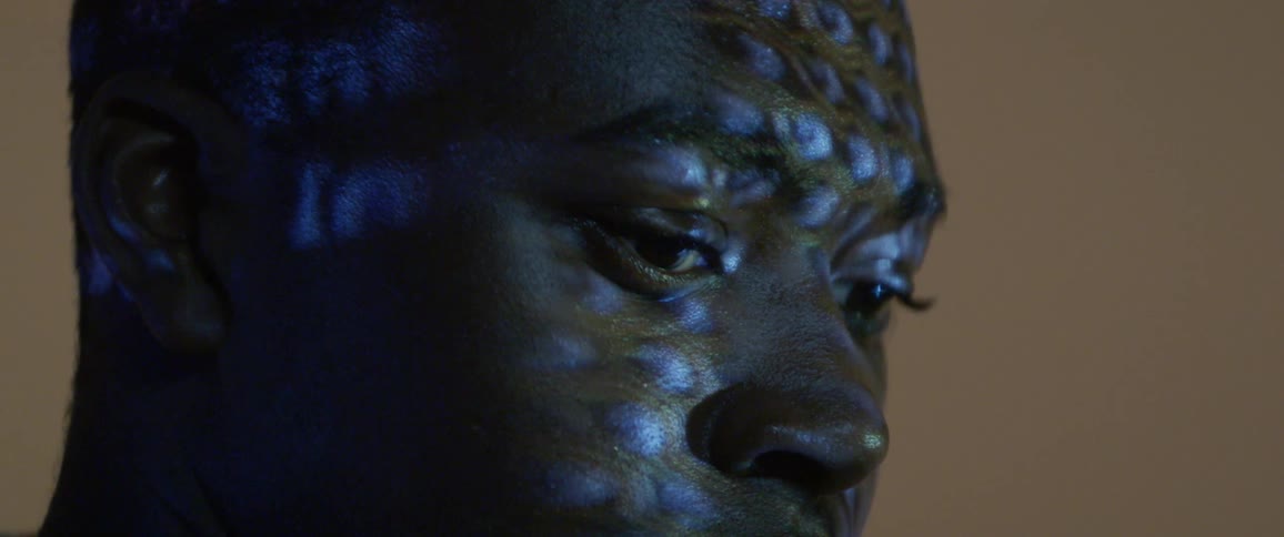A black male teenager looks at a screen as the lights reflect on his face