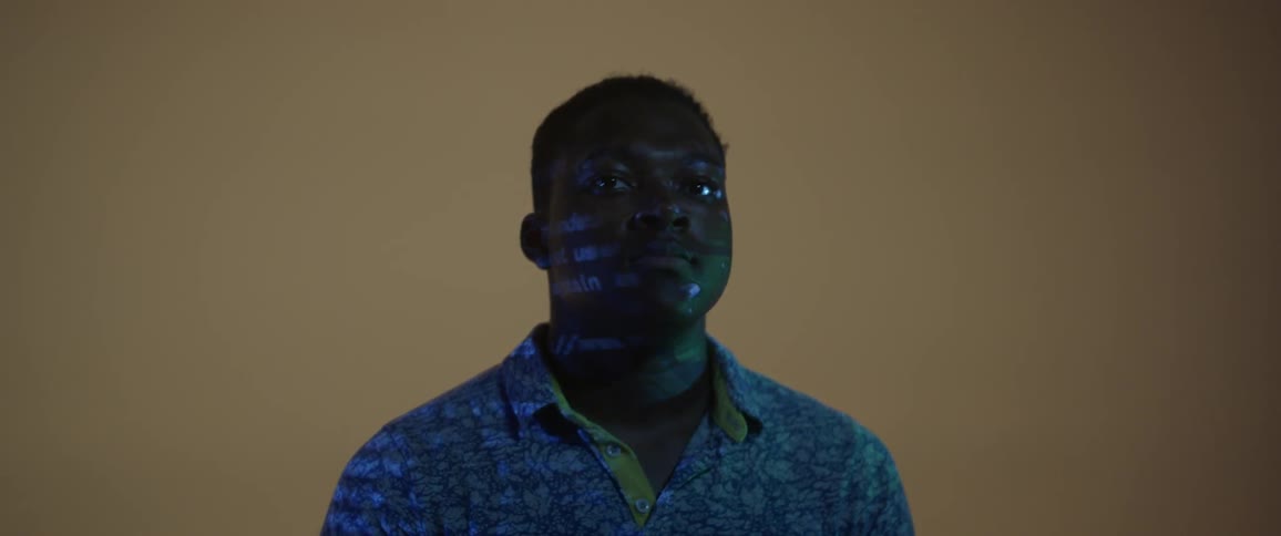 A black male stands indoors as computerized text is projected onto his face