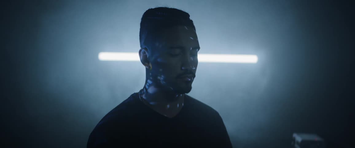 A man stands with eyes closed as lights and text flash across his face
