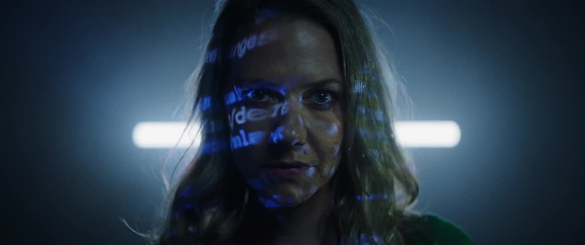 A woman stares into the camera while words are projected onto her face