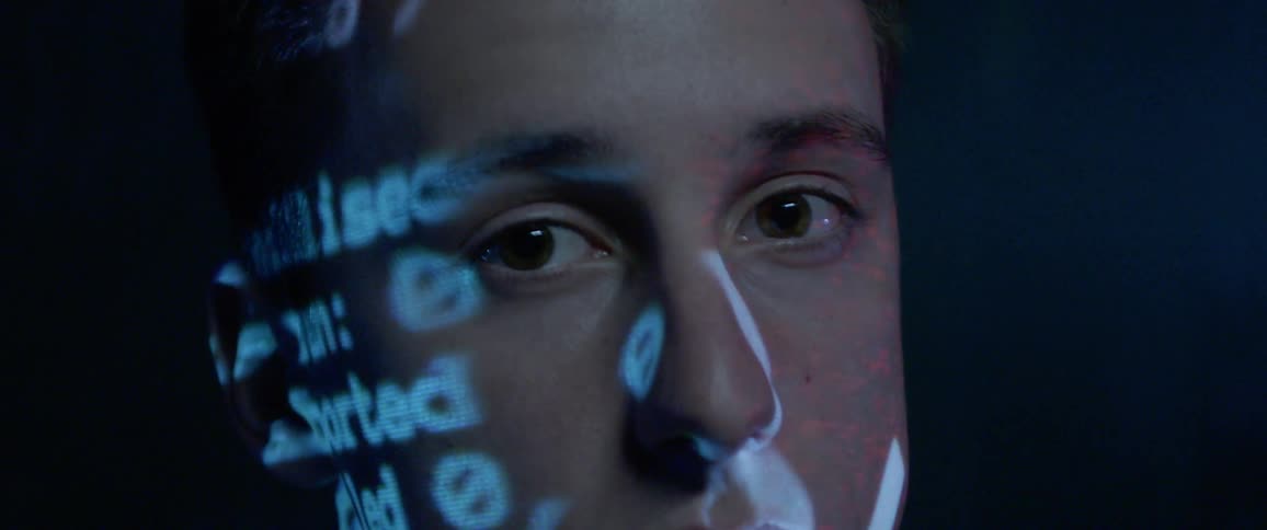 A man looking in the camera ascomputer code is projected onto his face