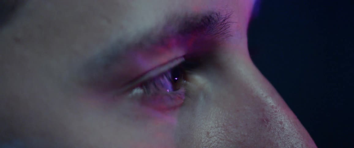 Close up of a young man while he watches a screen with bright lights on it