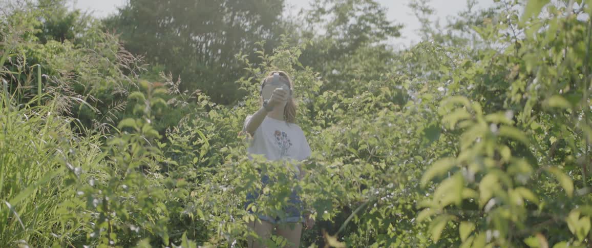 A young girl stands in the bushes and plays with a virtual reality device