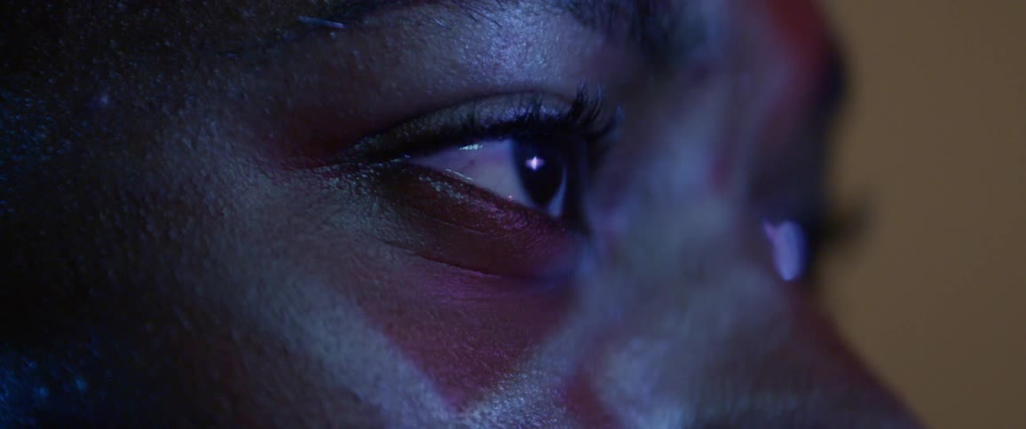 A black teen closes his eyes as he looks at a screen