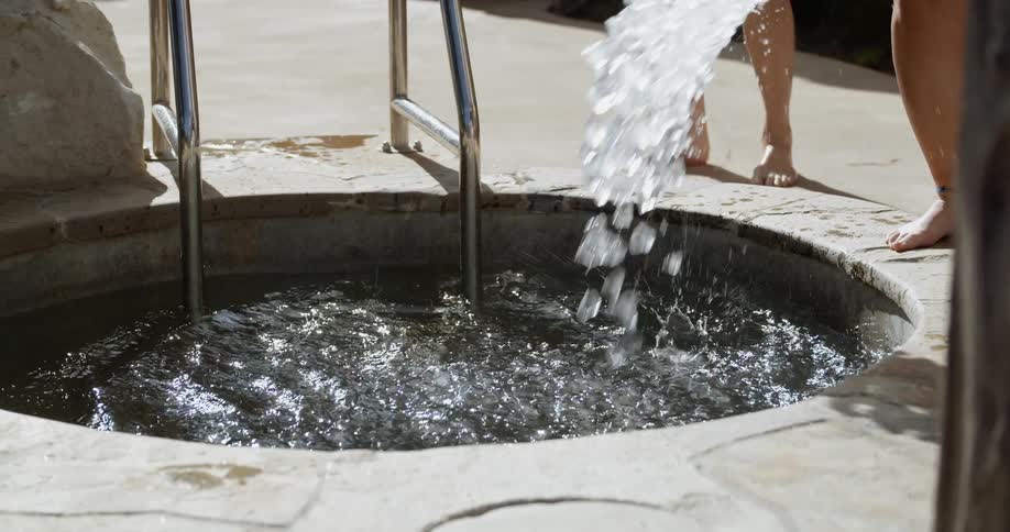A woman pours a bucket of ice into a hot tub