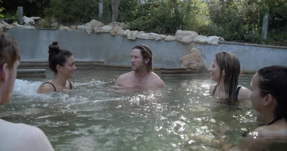 A group of people relaxing in a kind of thermal bath surrounded by bushes