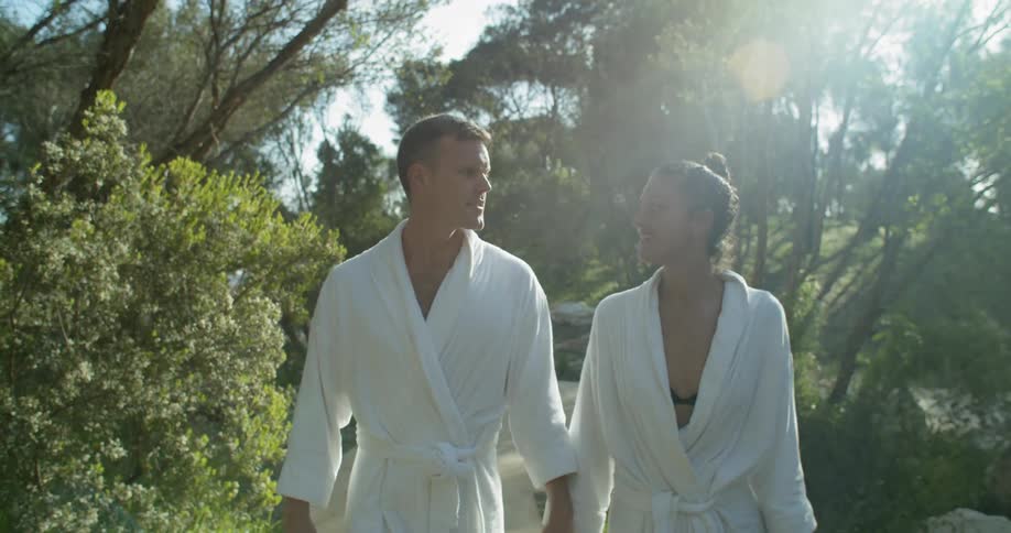 A man and a woman wearing white robes holding hands walking on a pathway outside