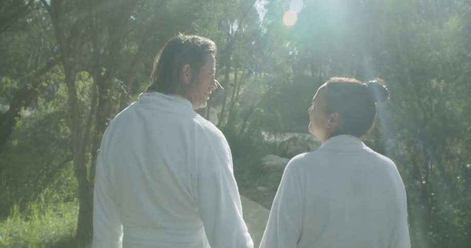 A couple walk down a path holding hands wearing robes