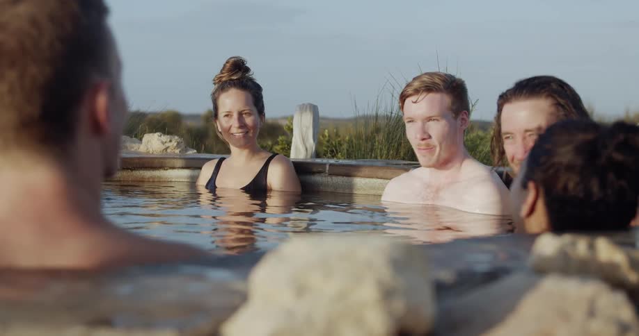 A group of people are all sitting in an outdoor spa while chatting on a sunny day