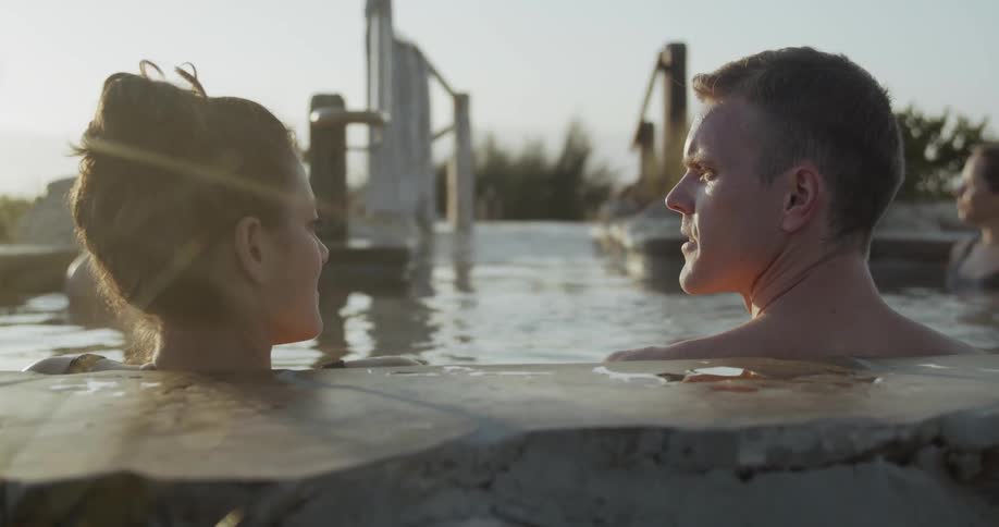 A group of people relaxing in a kind of thermal bath surrounded by bushes