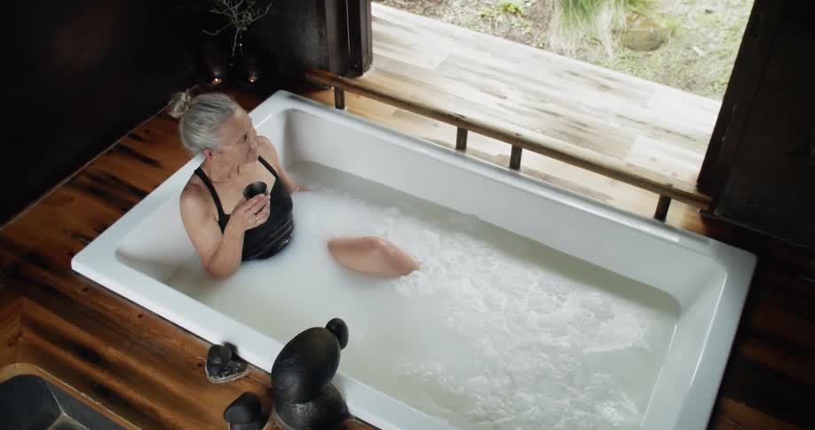 Woman relaxing with a drink in a milk bath looking out at a spa