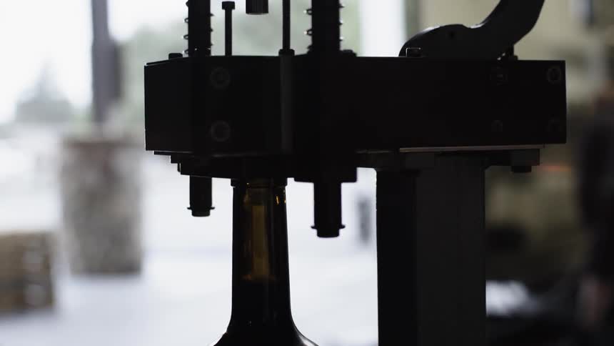 A person places a wine bottle on a machine to place a cork inside