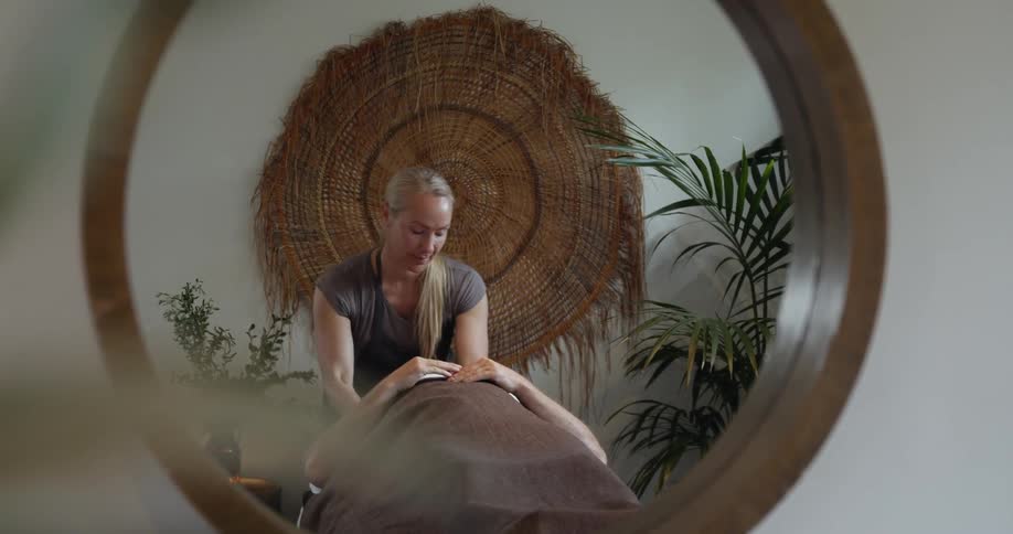 A woman lies on a massage table as another woman massages her