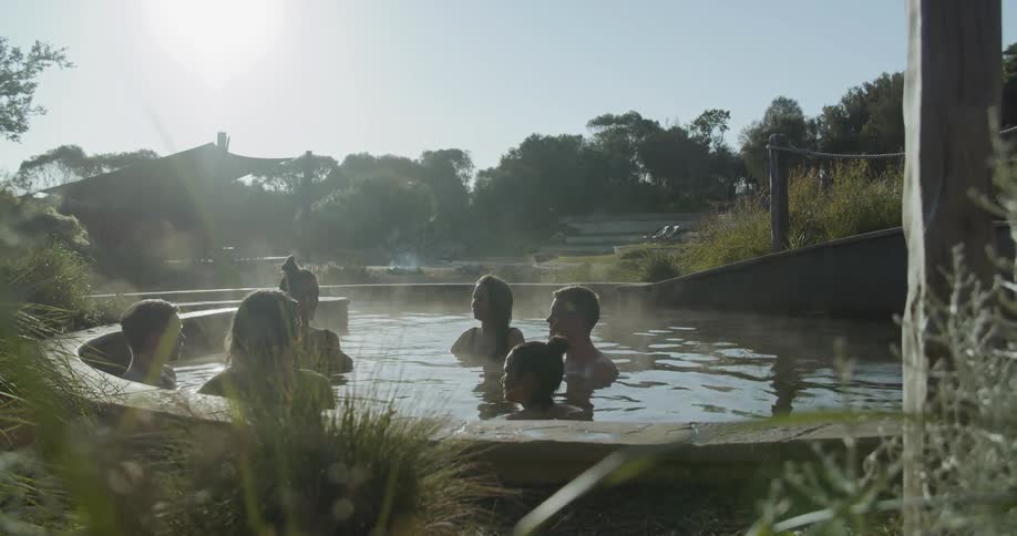 A group of six people relaxing in a kind of thermal bath surrounded by trees