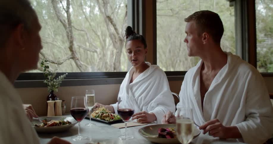 A man and woman sit together eating a meal wearing robes