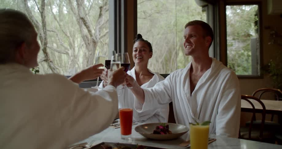 Four people wearing white robes are toasting with white glasses while meals sit in front of them at a table in a restaurant