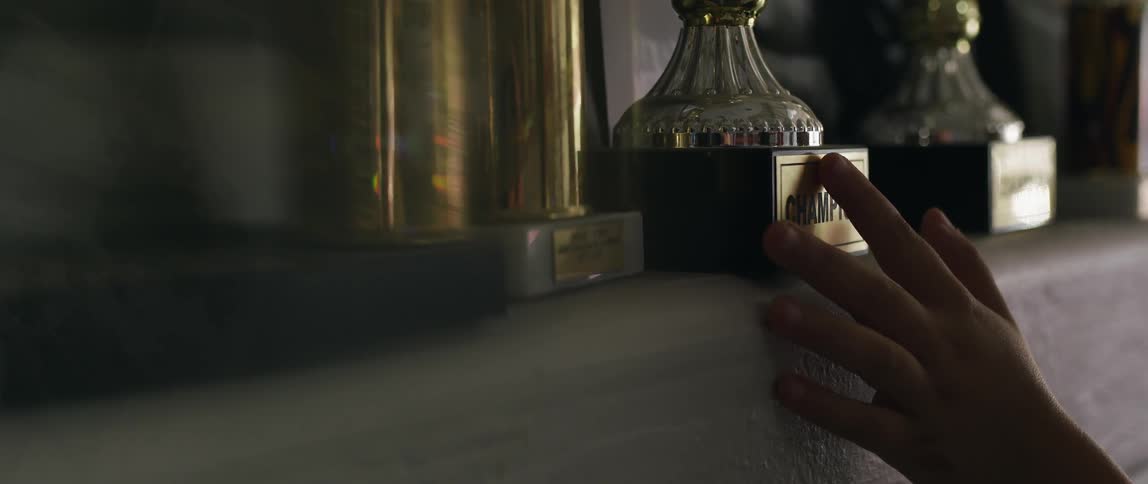A person runs their hand along one trophy in a line of trophies