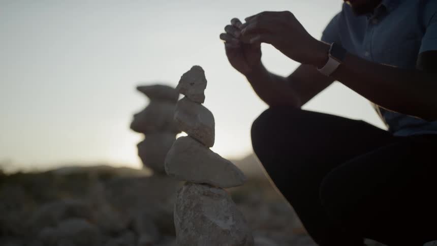 Man stacks rocks carefully as the sun rises