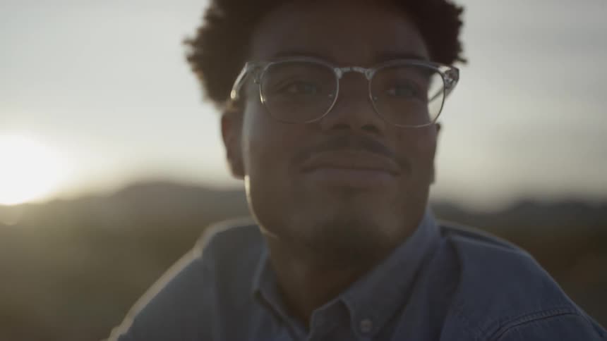 A young black male sits outside and smiles as the sun sets behind him