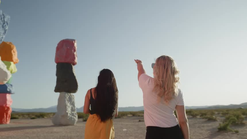 Three woman walking in the desert next to multiple colored tall rock monuments