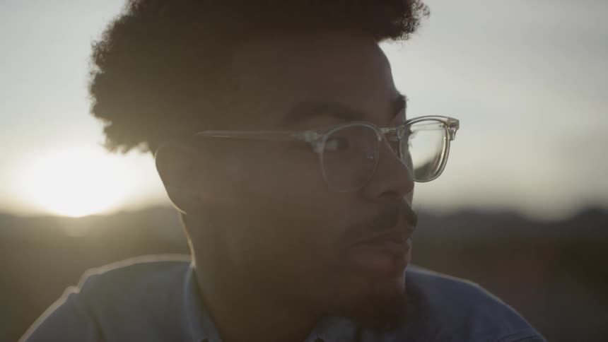 A young man sitting outdoors turning his head to smile into the camera
