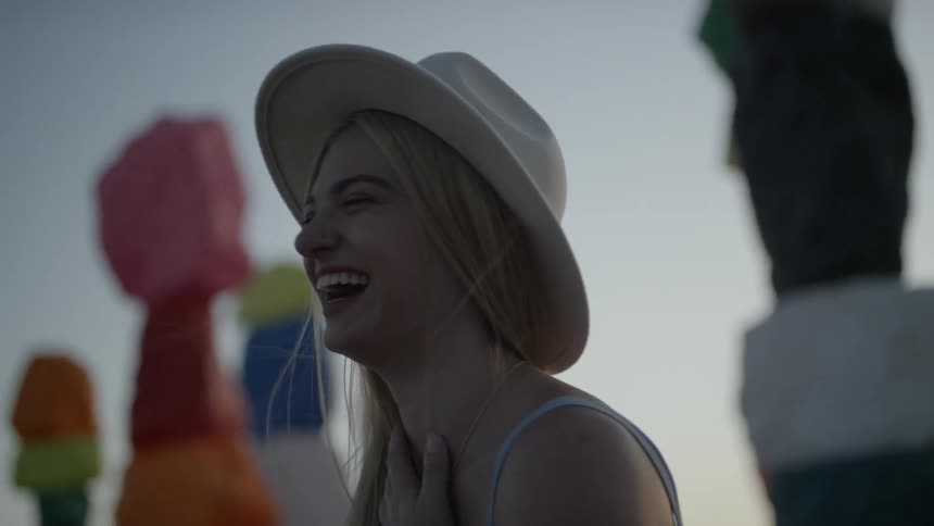 A young woman laughing while standing outdoors in the evening near columns of colored stones