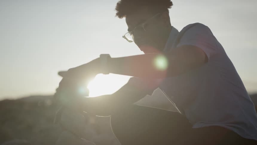 Black man wearing glasses puts stones on top of each other at sunset