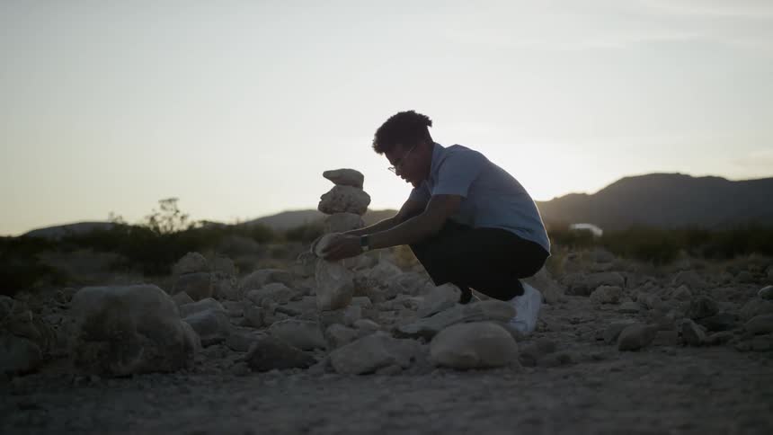 A young man stacking stones in the desert