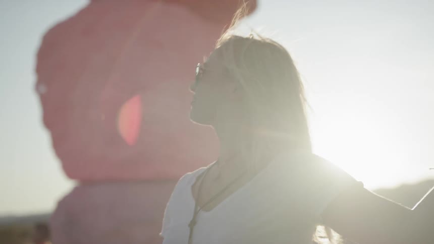 A white woman wearing sunglasses touches a rock while looking around her surroundings