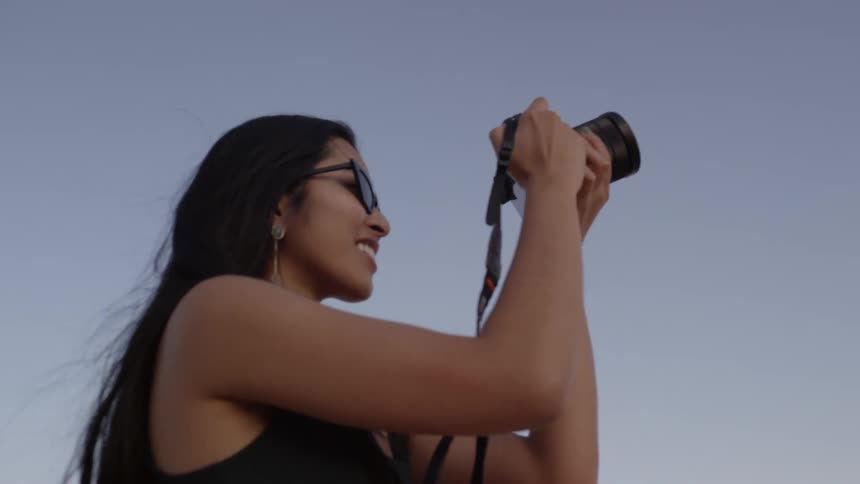 Asian woman wearing sunglasses takes a picture of colorful stone pillars at dusk