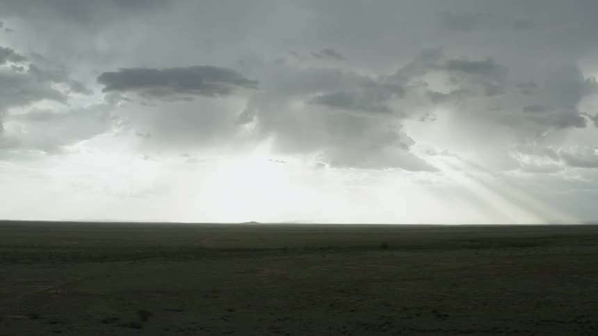 Sunlight shines through gray clouds over green fields