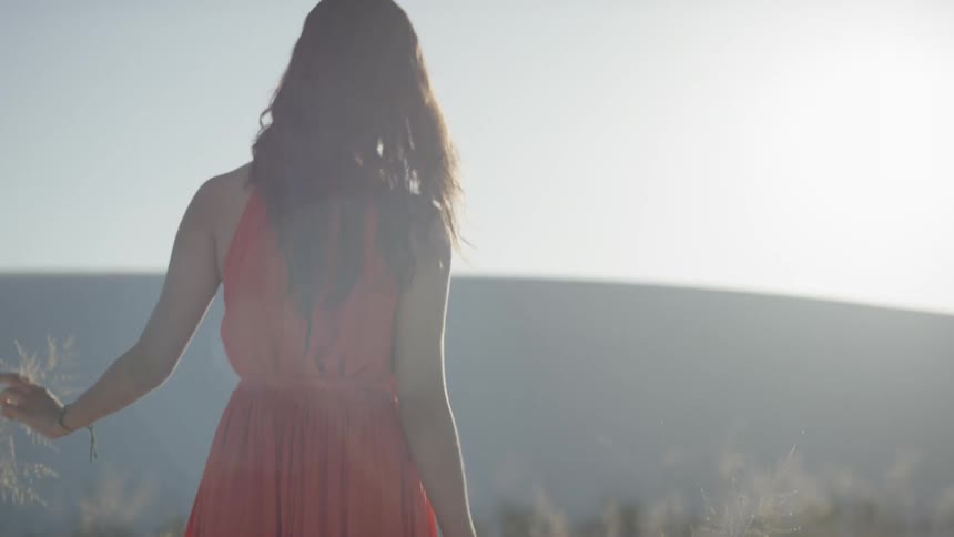 Brunette woman wearing a red dress walks on the white sand desert and touches dry plants
