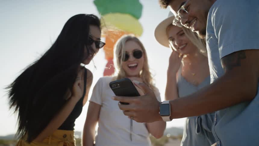 A group of friends standing near the painted rock towers in the desert laugh as they look at photos on a phone