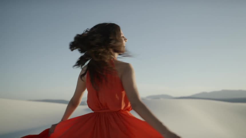 Brunette woman wearing a red dress turns around happily on the white sand desert