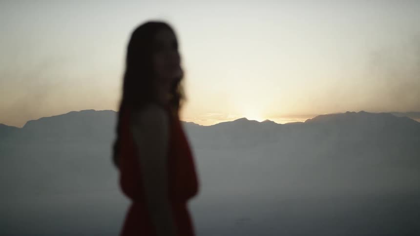 A woman in a red dress turning her head from the sunrise to look at the camera