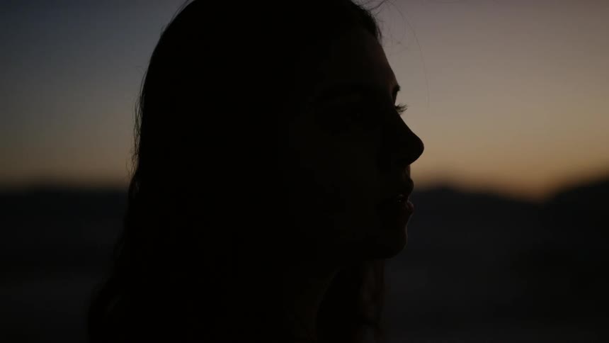 The silhouette of a young woman is seen against the backdrop of a mountain range at sunset